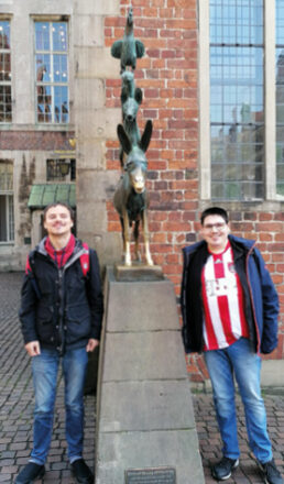 Zwei junge Männer mit Behinderung stehen neben den Bremerstadtmusikanten in der Bremer Innenstadt.
