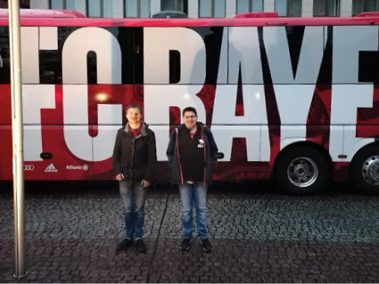 Zwei junge Männer mit Behinderung stehen vor dem FC Bayern Team-Bus.