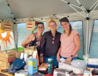 3 Damen stehen lächelnd in einem Tombola-Stand.