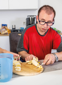 Ein junger Mann mit Behinderung schneidet eine Banane.